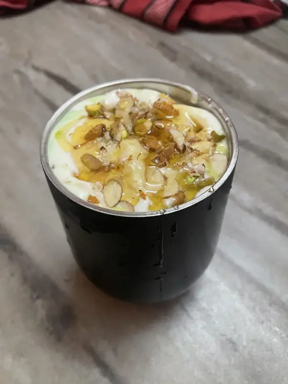Avocado ice cream milkshake in a steel tumbler, topped with chopped almonds, pistachios and a honey drizzle