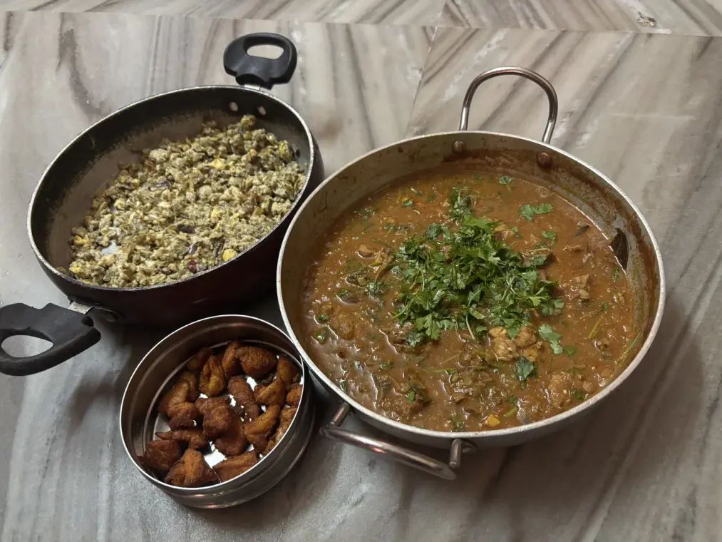 Chicken chettinad gravy heaped with fresh coriander, beside a pan of egg scramble and a tin of chicken 65