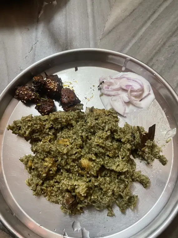 A plate of donne biryani with a few sesame-glazed chicken pieces and sliced onions in curd