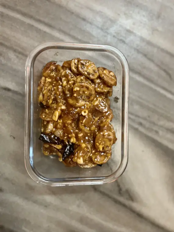 A glass box of glazed lotus stem with sesame seeds, garlic and dried chillies