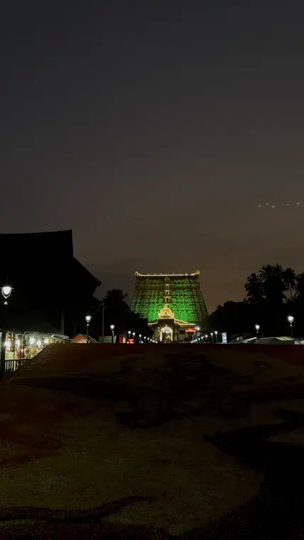 The Padmanabhaswamy temple tower lit green and gold against a dusky night sky, lamp posts lining the path