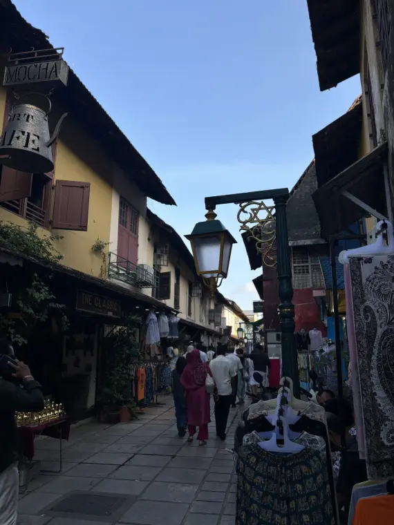 A narrow street in Jew Town, Fort Kochi: yellow tiled-roof houses, a hanging kettle cafe sign and an old lamp post
