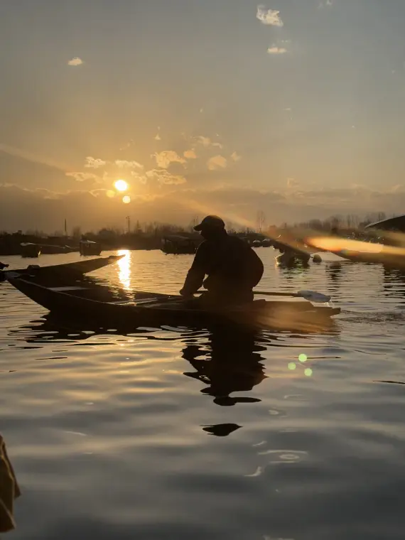 A boatman silhouetted in a shikara on Dal Lake, the low sun flaring gold across the water