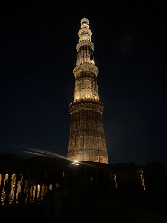 Qutub Minar lit up at night, looking straight up the tower from the ruins at its base