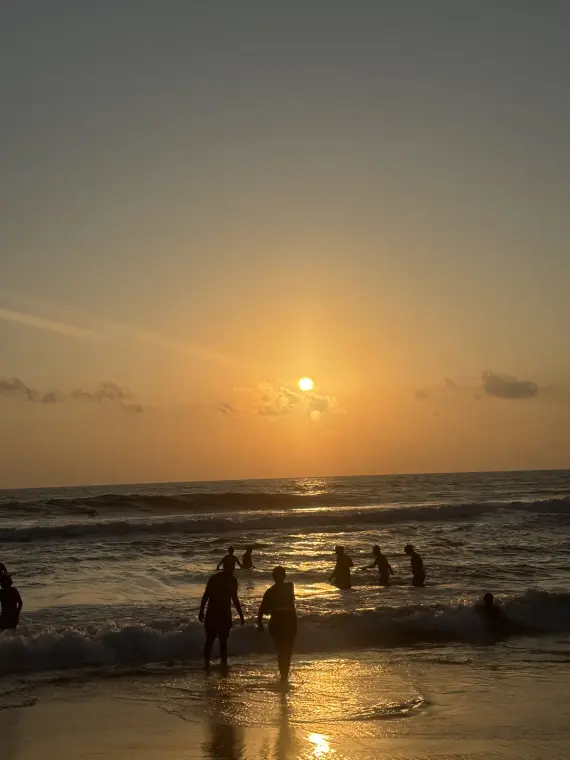 Silhouettes of people wading into the waves as the sun sets over the sea