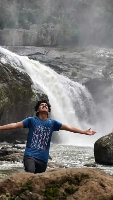 Mariappan with arms flung wide, looking up at a roaring waterfall