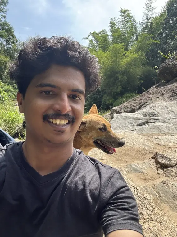 A smiling selfie on a rocky trail, with a friendly brown dog peeking over his shoulder